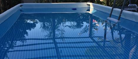 A clear blue swimming pool with a tiled deck, surrounded by a pergola structure.