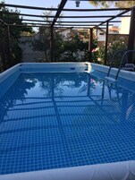 Una piscina azul cristalina con una solana con baldosas, rodeada por una estructura de pérgola.
