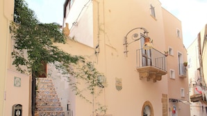 A narrow street with a building featuring a tiled staircase and a balcony with a hanging light fixture. - Conte Luna (Sciacca)