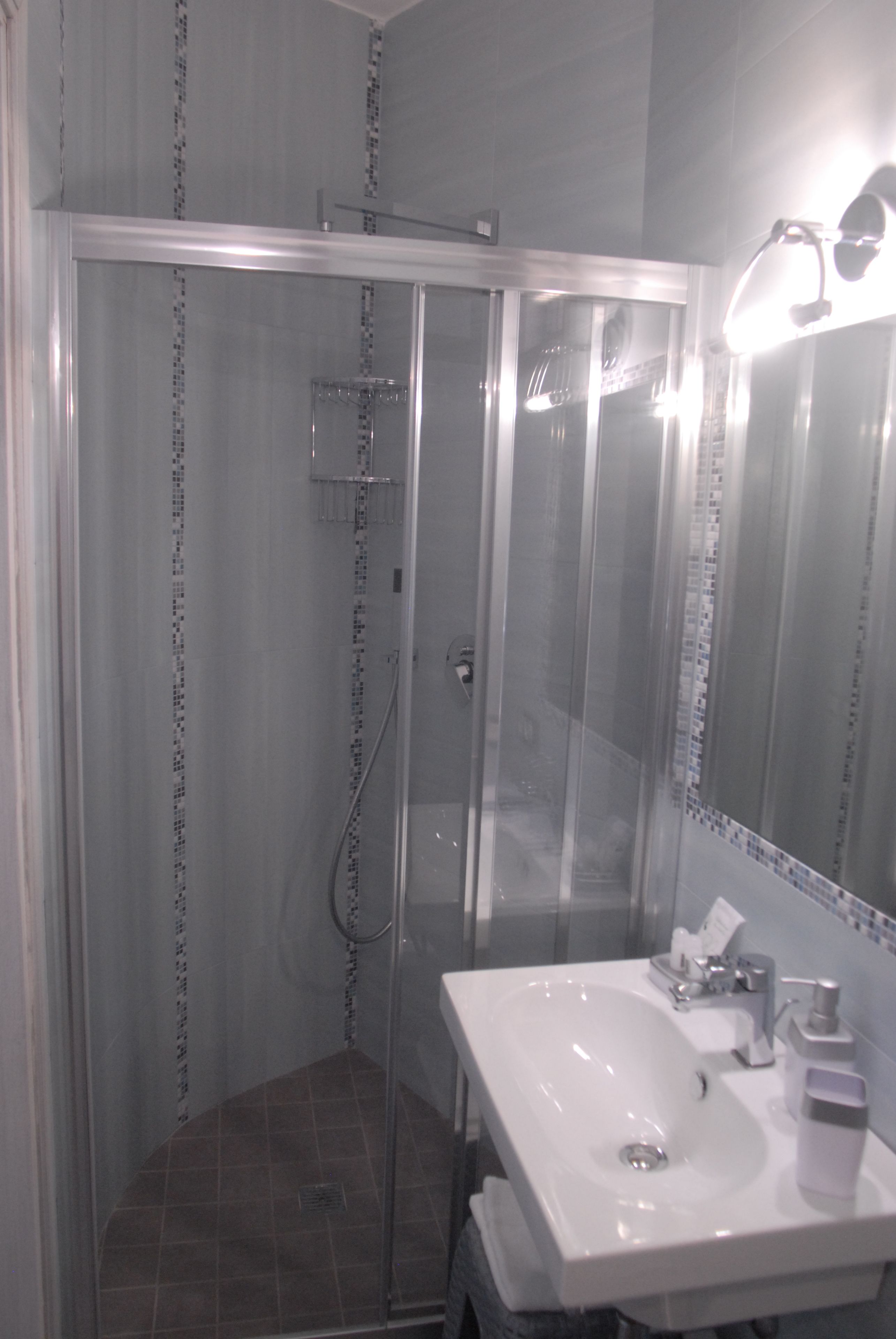 A bathroom with a glass-enclosed shower, a white sink, and a mirror with lights.