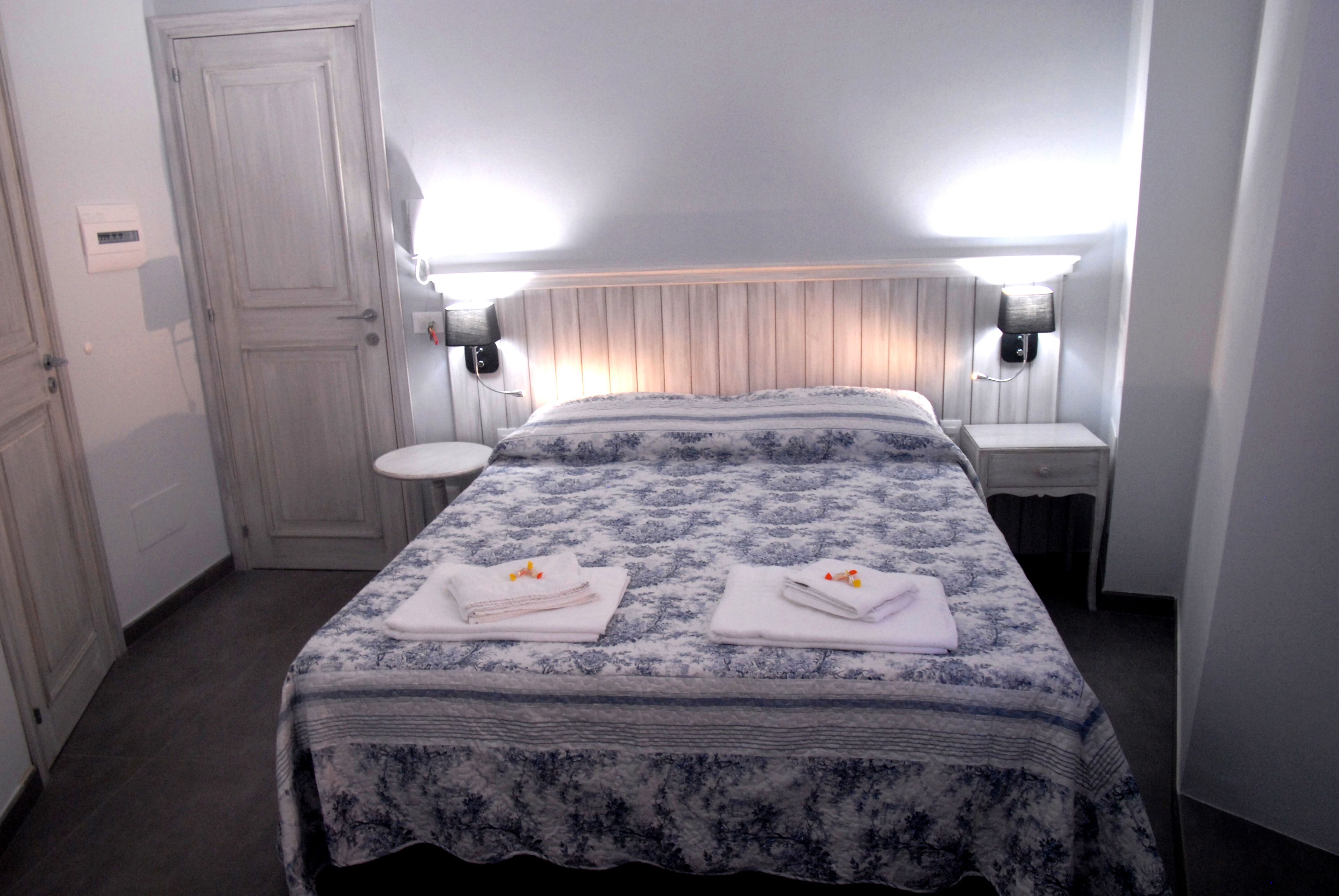 A bedroom with a bed, two bedside tables, a nightstand, a door, and a light switch on the wall.