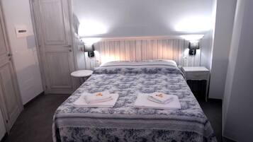 A bedroom with a bed, two bedside tables, a nightstand, a door, and a light switch on the wall.