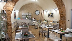 A restaurant with a rustic stone archway, white tables, and chairs, and a clock on the wall. - Conte Luna (Sciacca)