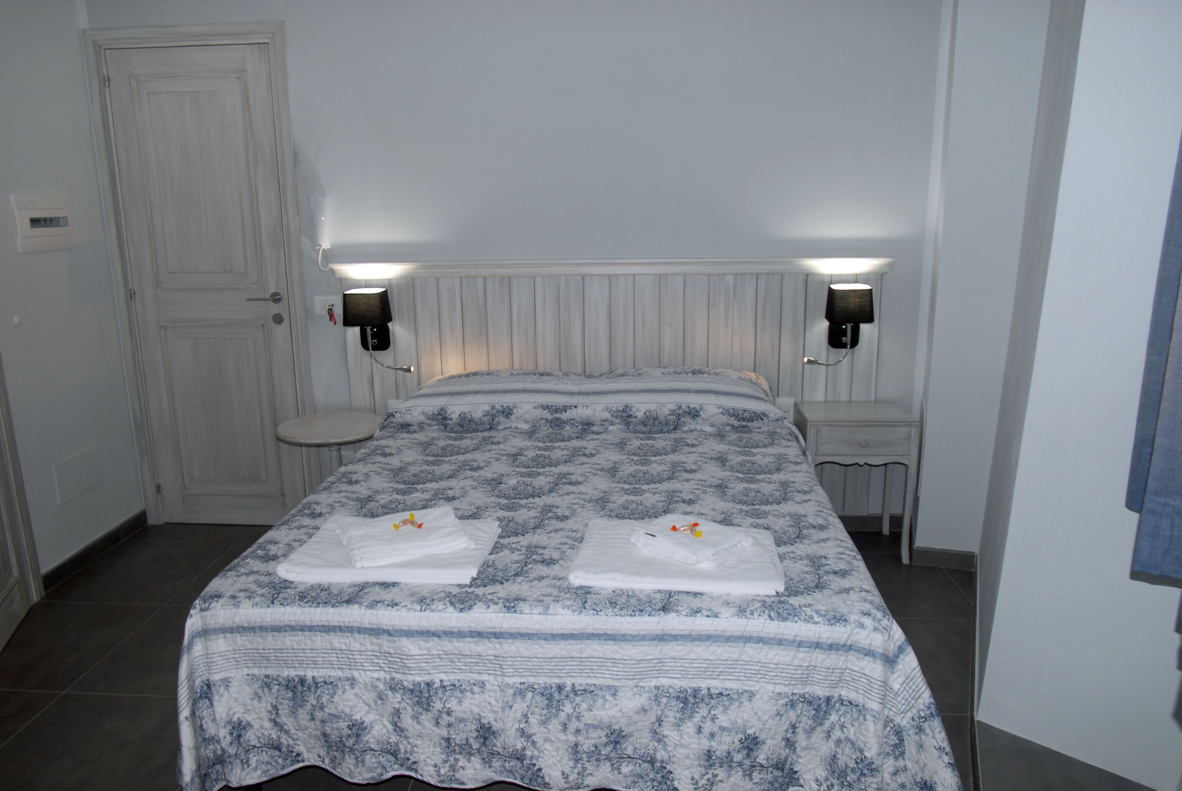 Une chambre d’hôtel avec un lit, deux tables de chevet, une porte blanche et une lampe fixée au mur.