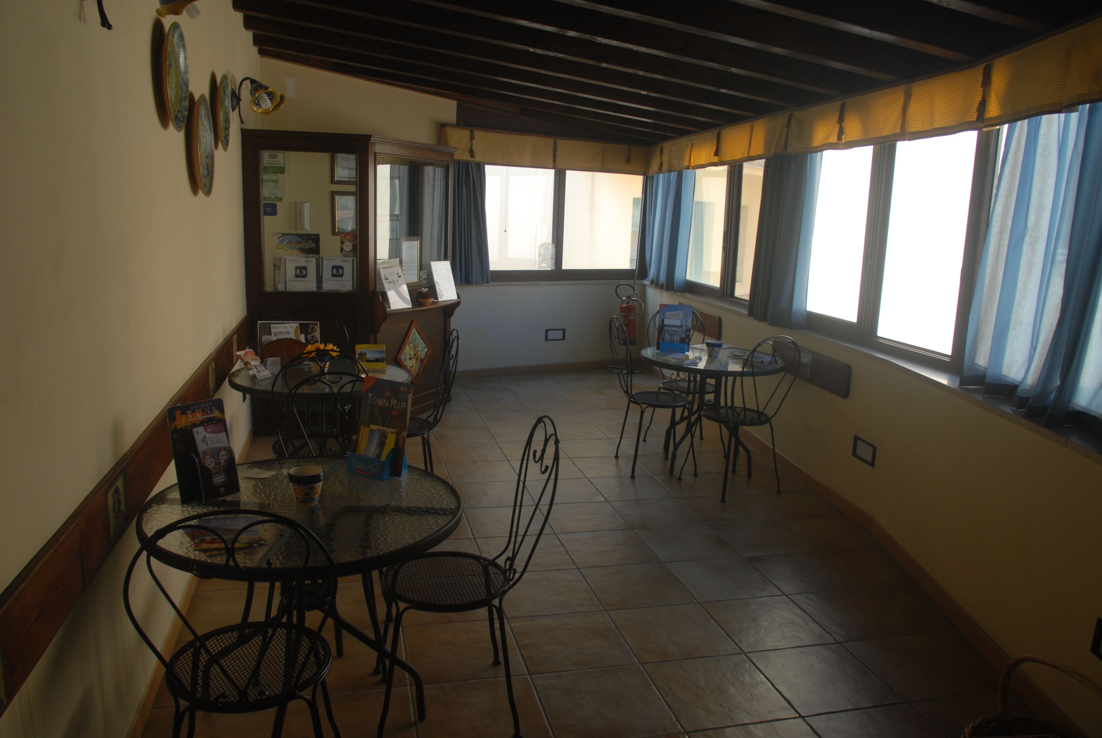 A dining area with round tables and chairs, a tiled floor, and large windows with curtains.