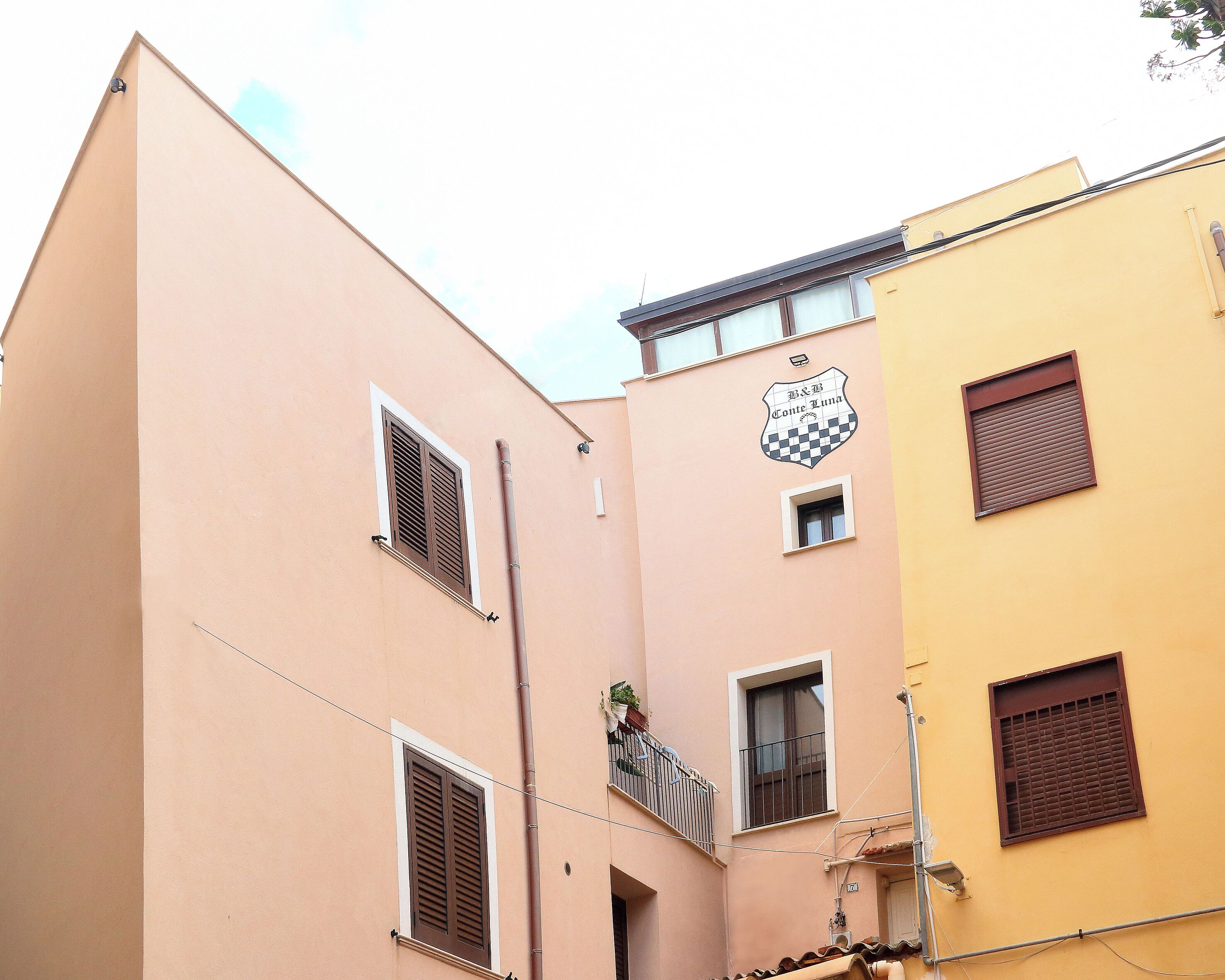 A building with a checkered emblem and a balcony with a potted plant.