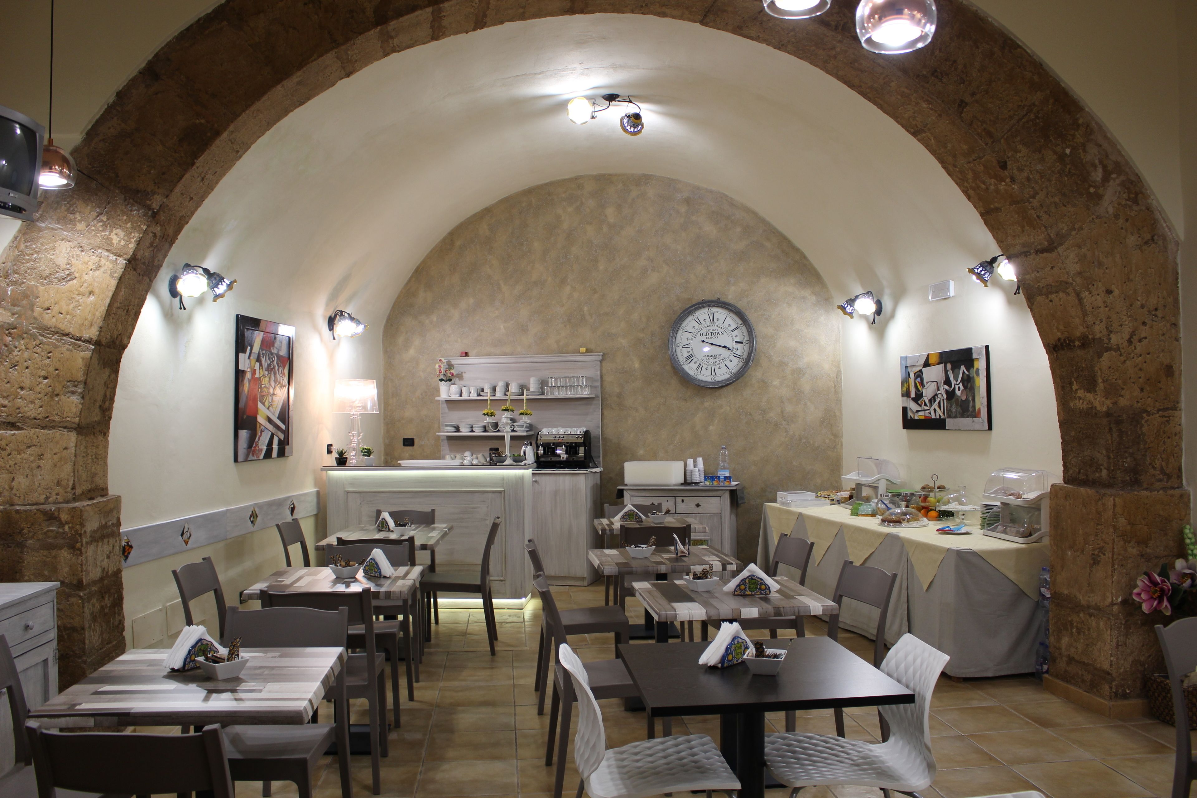 A restaurant with a rustic stone arch ceiling, multiple tables and chairs, a clock on the wall, and a bar area with various items.