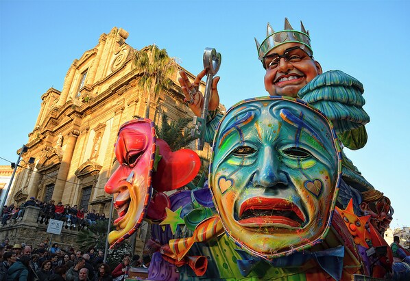 A colorful, ornate building with classical architecture, a crowd of people, and a large, vibrant sculpture.