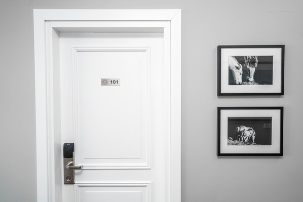 A white door with a digital lock and a number plate reading "101". Two black-and-white framed photographs are hung on the wall to the right. - Guesthouse Keflavik by Reykjavik Keflavik Airport (Reykjanesbær)