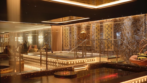 Un área de spa lujosa con un jacuzzi, asientos y una pared de mármol con diseños intrincados.