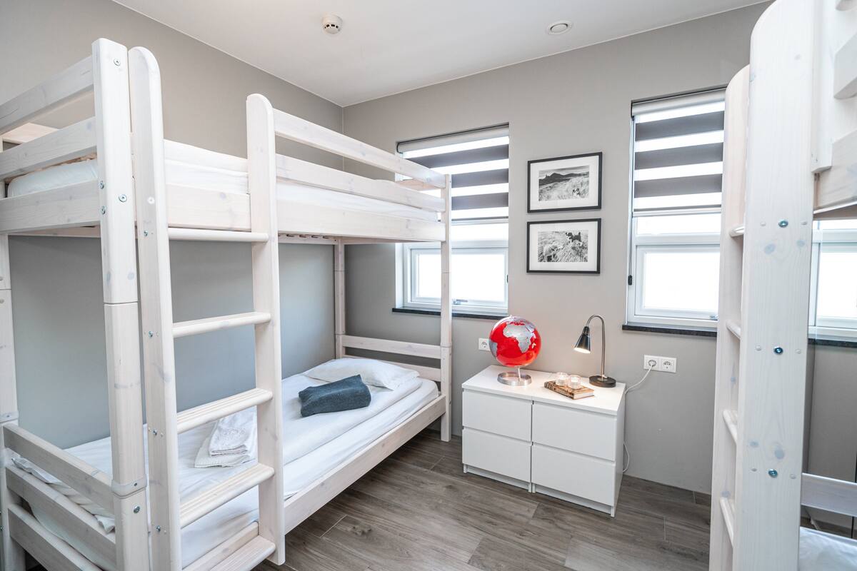 A bunk bed room with a desk and globe, featuring two windows and framed pictures on the wall.