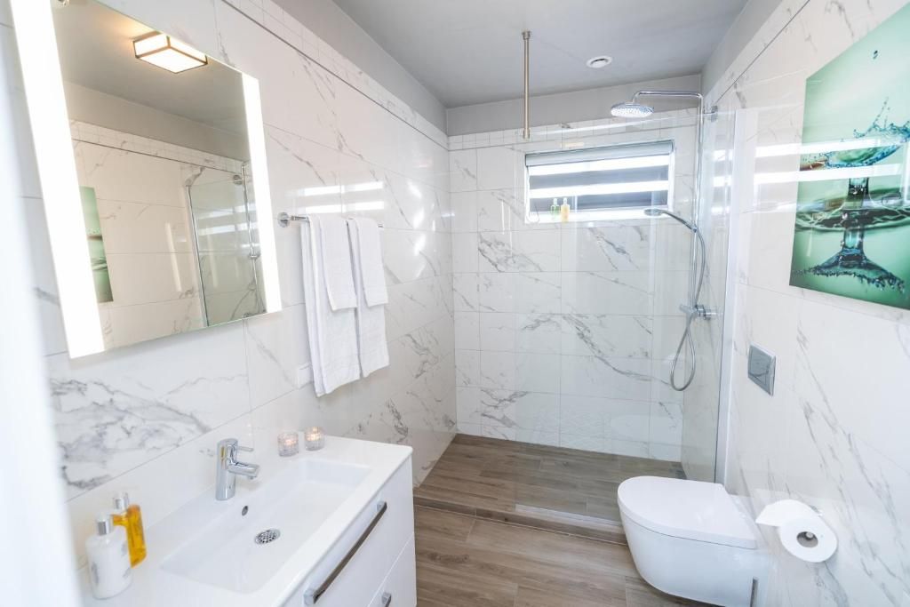 Een moderne badkamer met een marmeren wastafel, een douchecabine met glazen wanden en een toilet.