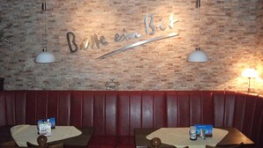 Interior de restaurante con pared de ladrillo, dos mesas con menús y una zona de asientos tipo cabina en rojo.