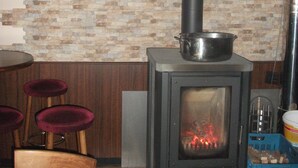 Una habitación con pared de piedra, un estufa de leña, una mesa con sillas y un baúl azul.