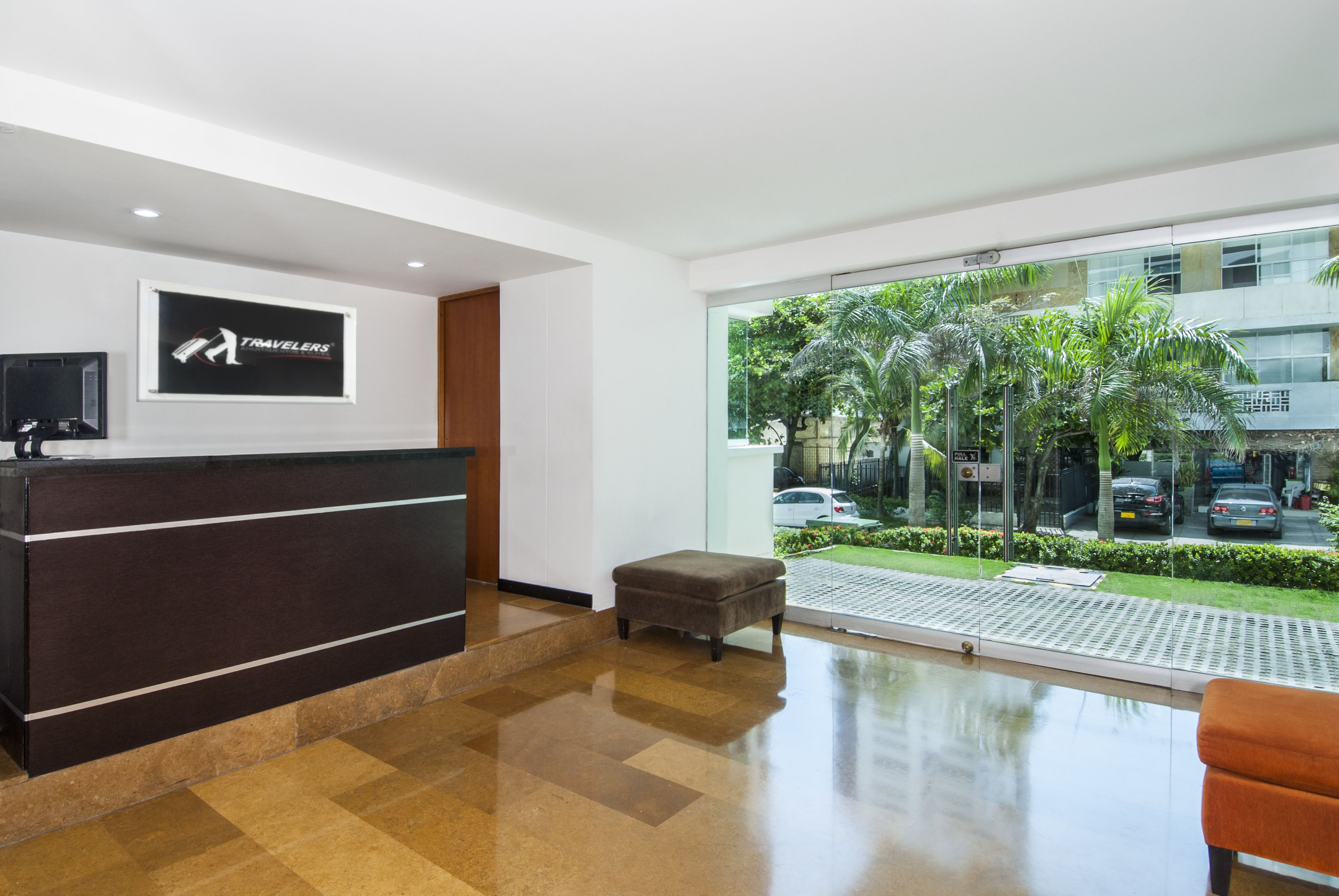 A reception area with a dark reception desk, a small ottoman, and a large window offering a view of palm trees and a parking lot.