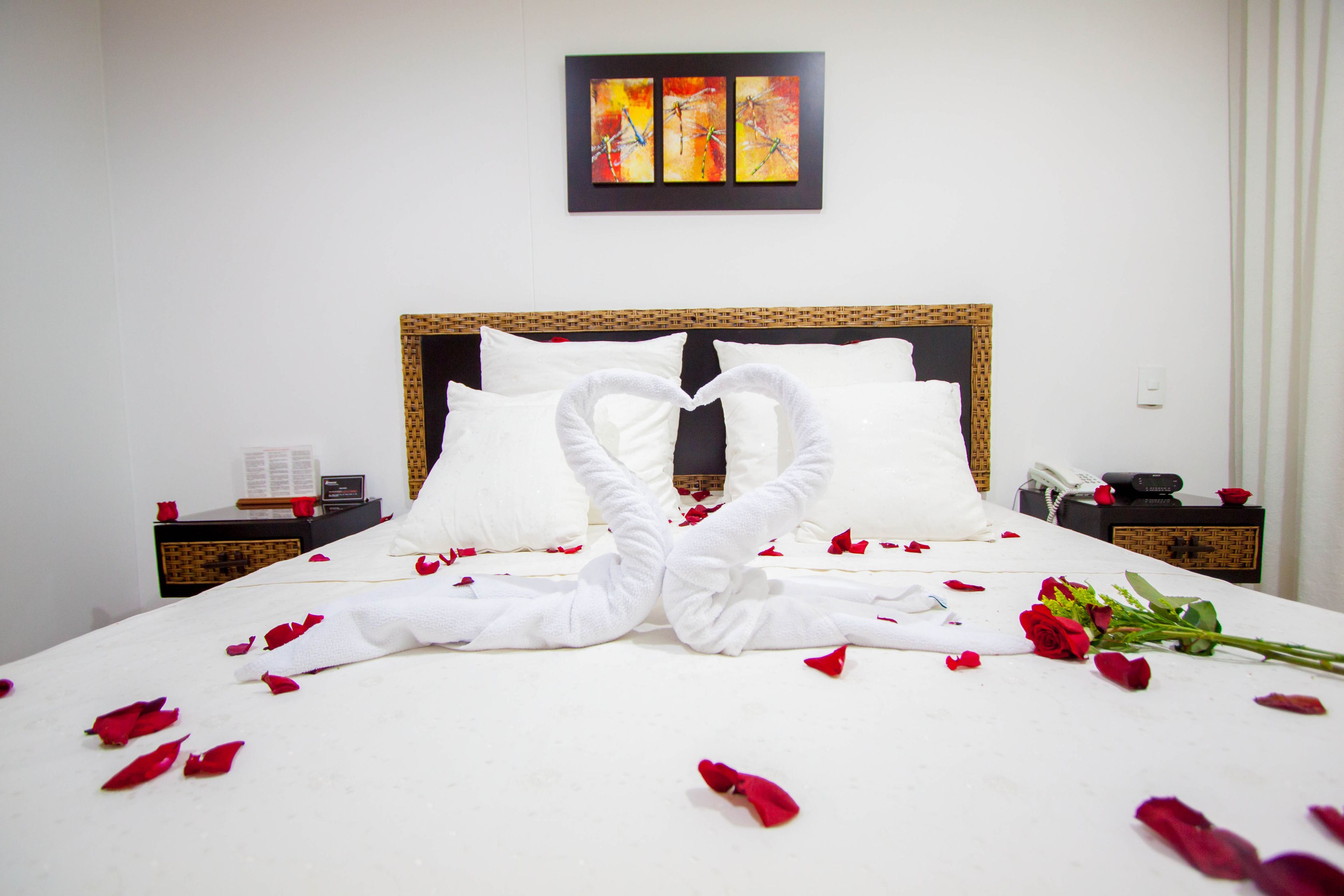 Una habitación de hotel con una cama bien hecha, un ramo de rosas rojas y una obra de arte enmarcada en la pared.