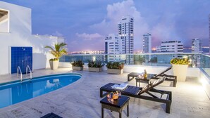 Un área de piscina en la azotea con sillones, una mesita y plantas en macetas.