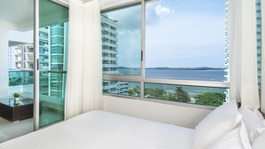 Habitación de hotel moderna con un ventanal que ofrece vistas al mar y edificios.