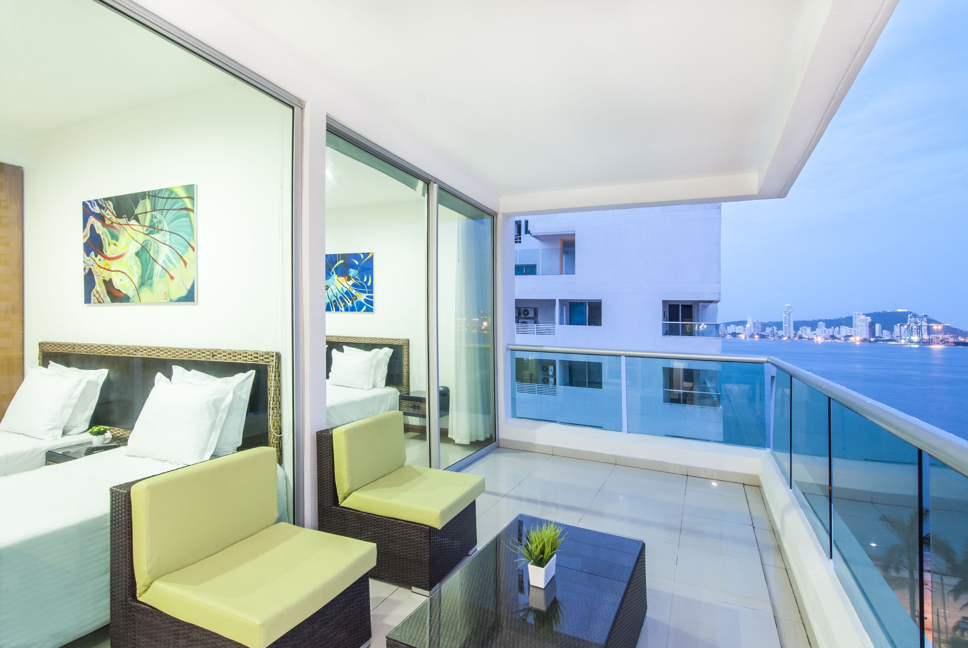 A modern hotel room with a balcony, a bed, two sofas, and artwork on the walls.