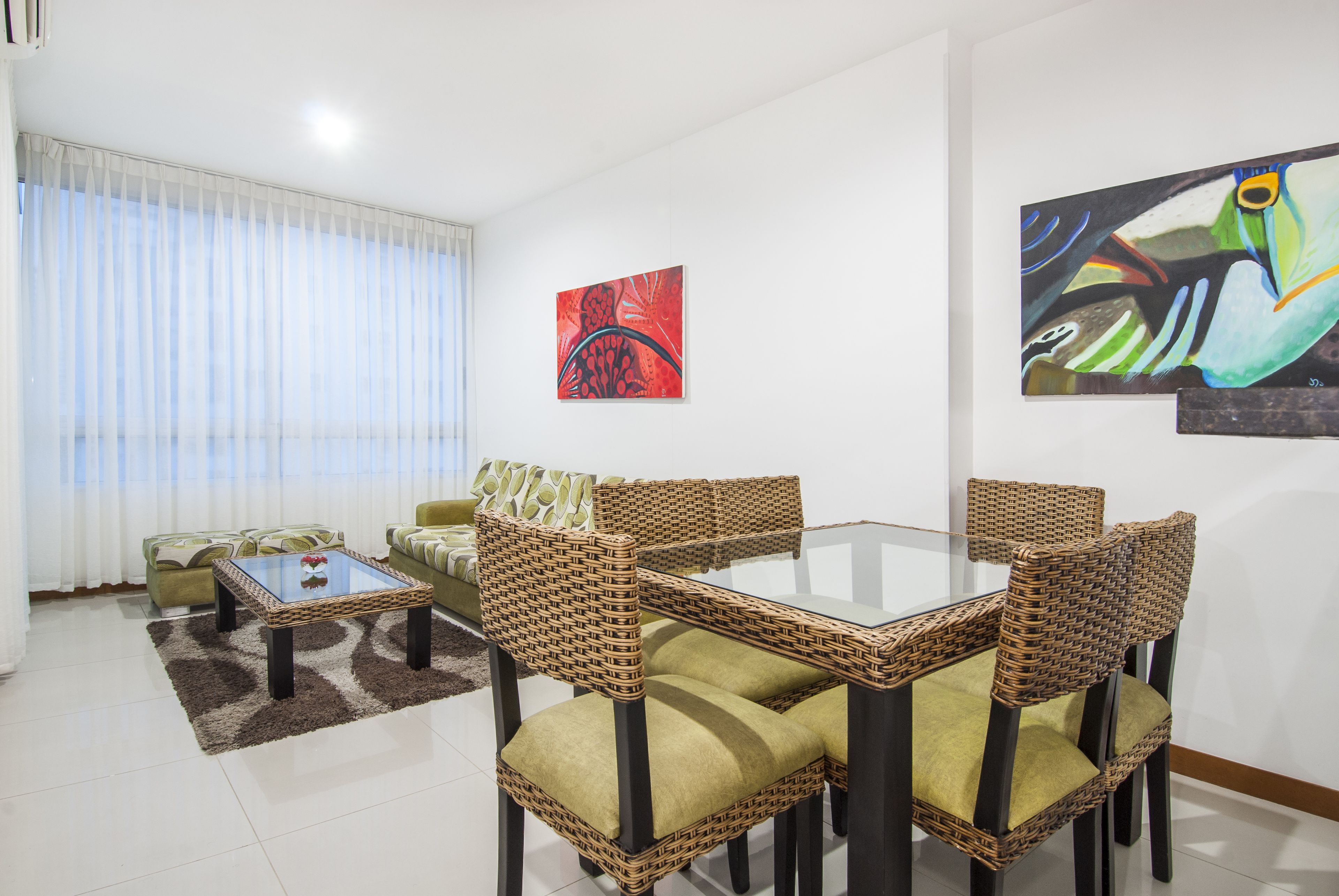 A living room with a glass-top table, wicker chairs, and green sofas.