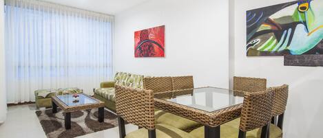 A living room with a glass-top table, wicker chairs, and green sofas.