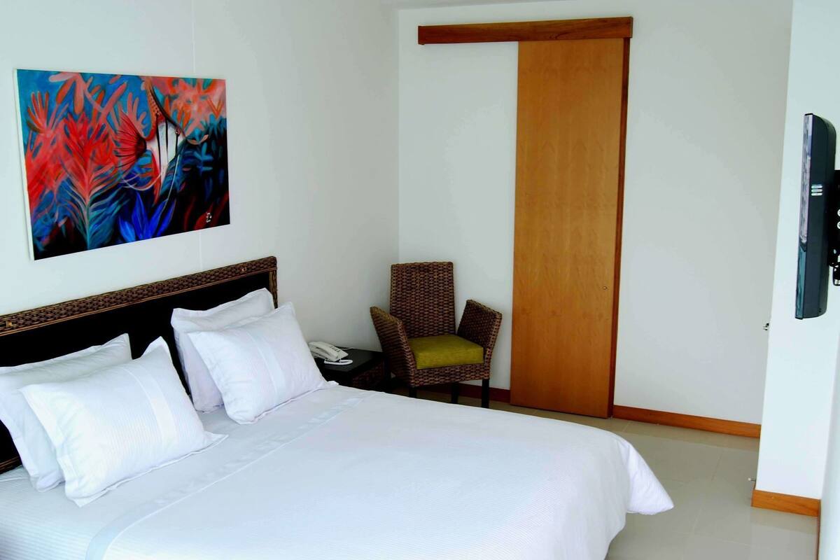 Een hotelkamer met een bed, een stoel, een schilderij en een deur.