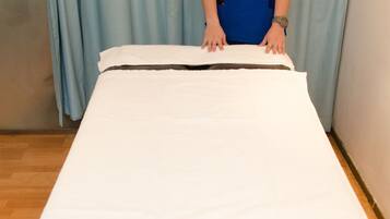 A person in blue scrubs standing behind a bed with a white sheet.