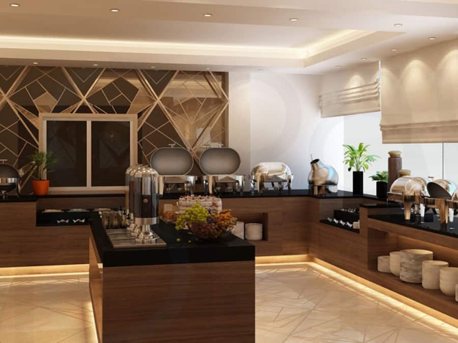 Un moderno vestíbulo de hotel con mostrador de recepción, zona de buffet y detalles decorativos como plantas e iluminación.