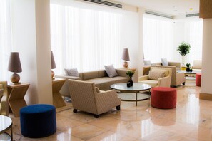 Ein modernes Wohnzimmer mit einem beigen Sofa, Sesseln, einem Couchtisch, Poufs und Lampen.