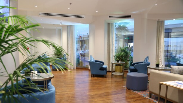 A modern hotel lobby with wooden flooring, blue seating, and large windows offering views of the street. - Dammam Palace Hotel (Dammam)