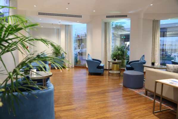 A modern hotel lobby with wooden flooring, blue seating, and large windows offering views of the street. - Dammam Palace Hotel (Dammam)