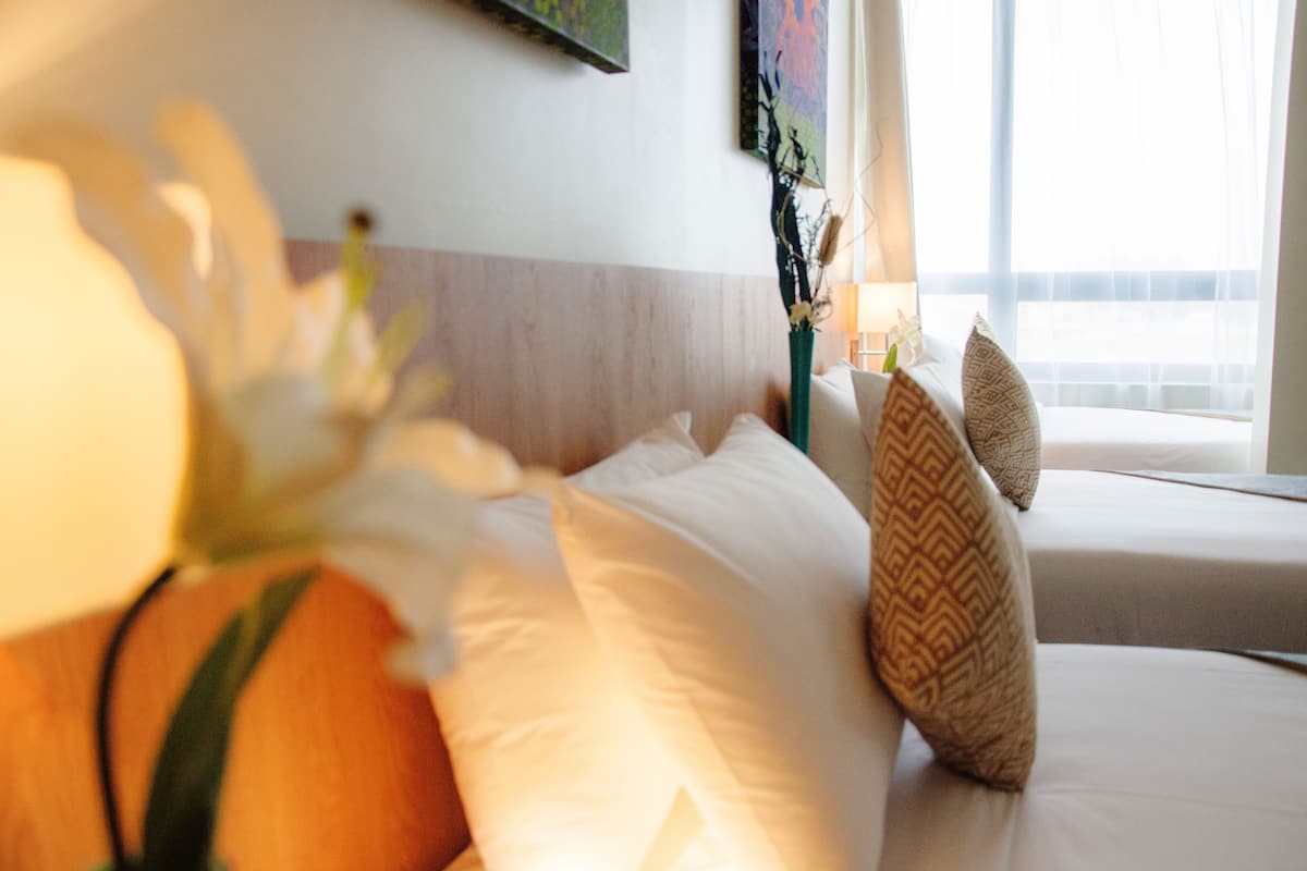 Quarto de hotel com cama, almofadas, um vaso com flores e um quadro na parede.