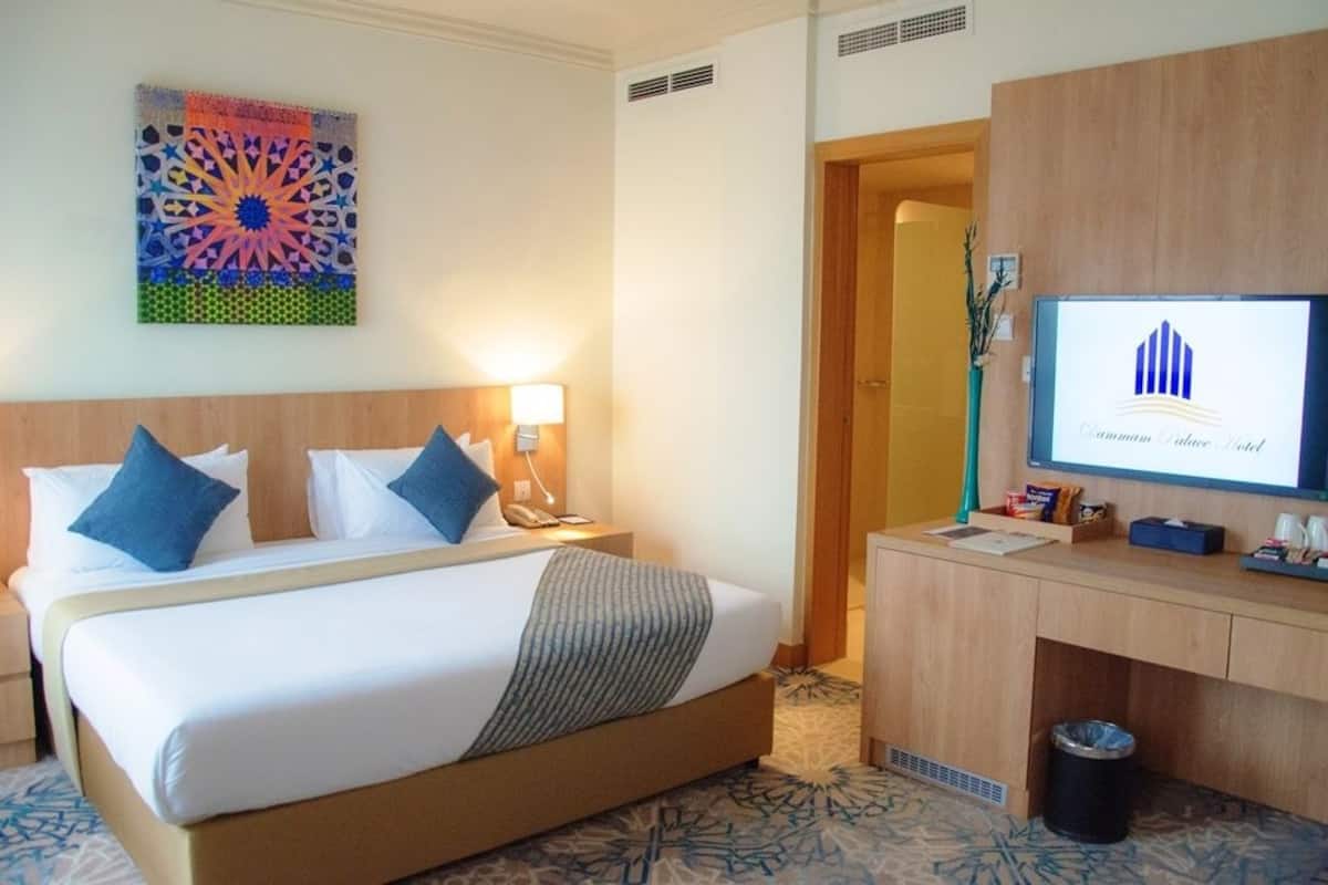 Quarto de hotel com uma cama, escrivaninha, computador e um objeto decorativo na parede.