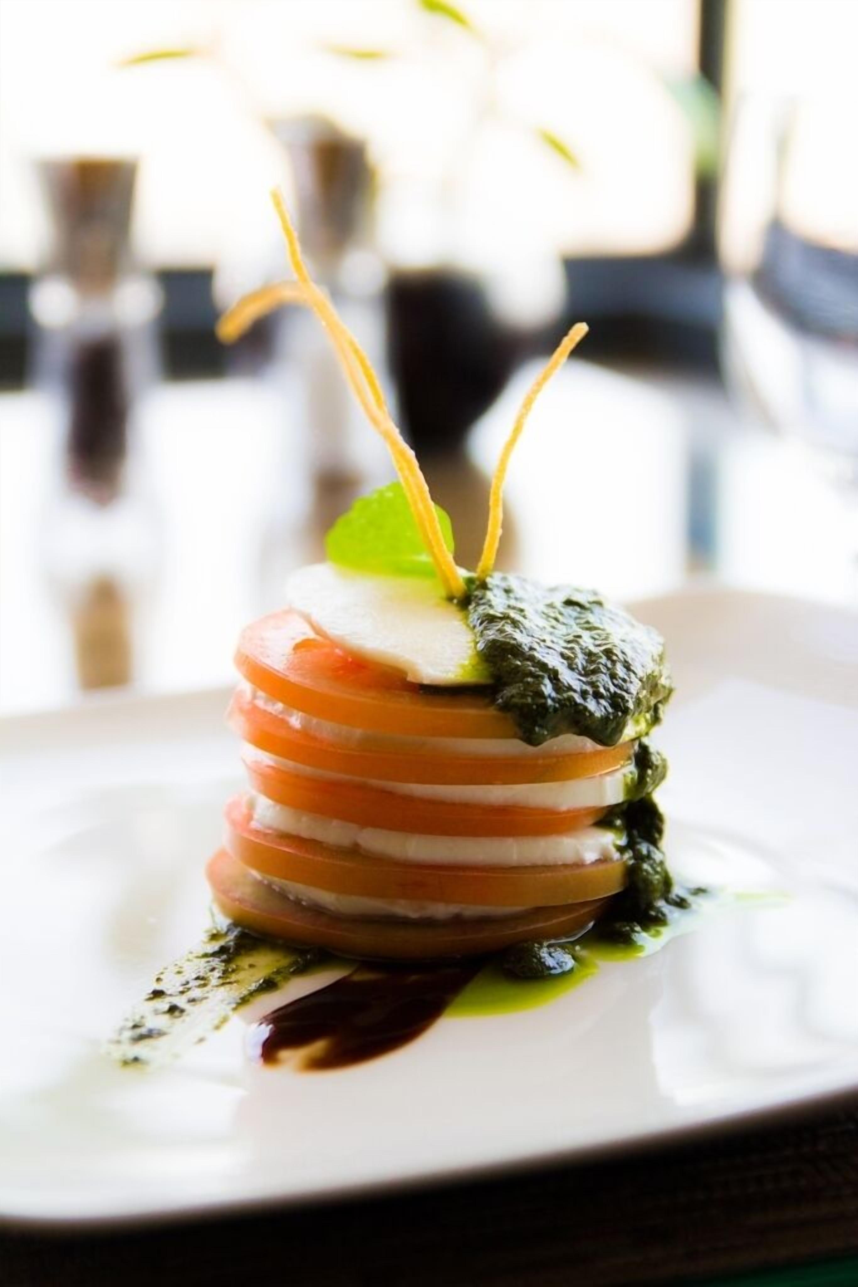 A plated dish with a layered presentation, garnished with a green leaf and a yellow edible element.