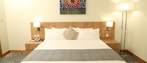Un cuarto de hotel con una cama grande, dos lámparas de noche, un teléfono y un cuadro abstracto y colorido en la pared.