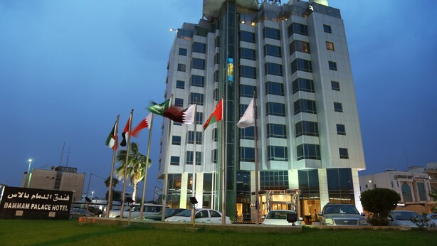 A hotel with multiple floors, a prominent sign at the top, and several flags in front. - Dammam Palace Hotel (Dammam)