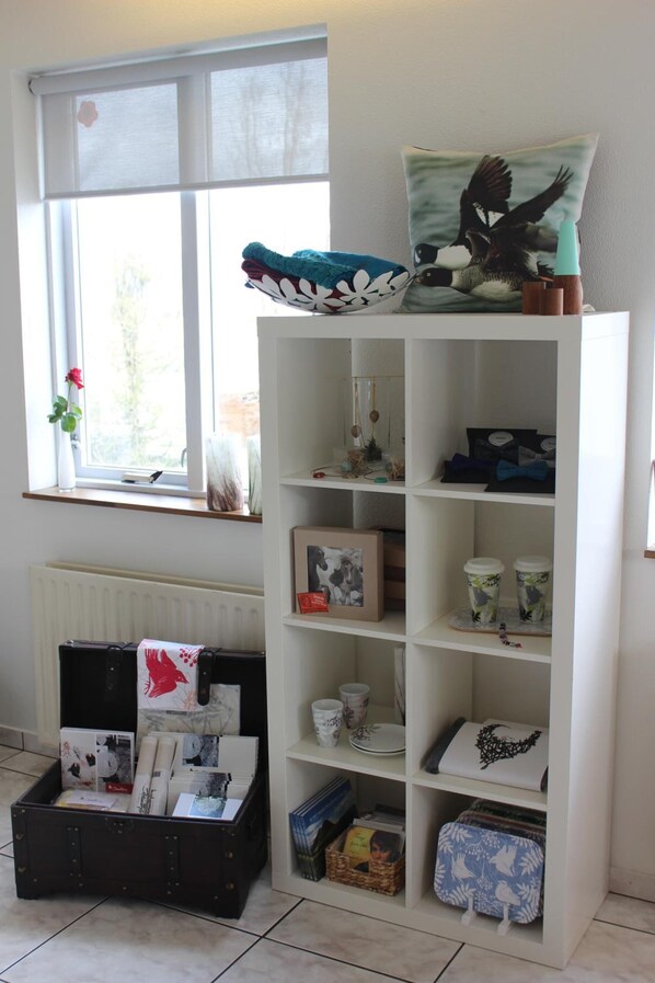 Una habitación con un estante blanco, una caja de almacenamiento negra y una ventana con vistas a follaje.