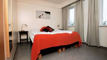 Una habitación de hotel con una cama, una mesita de noche, una lámpara, una ventana con cortinas y un cuadro en la pared.