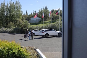 A parking area with a white car and a person with luggage.