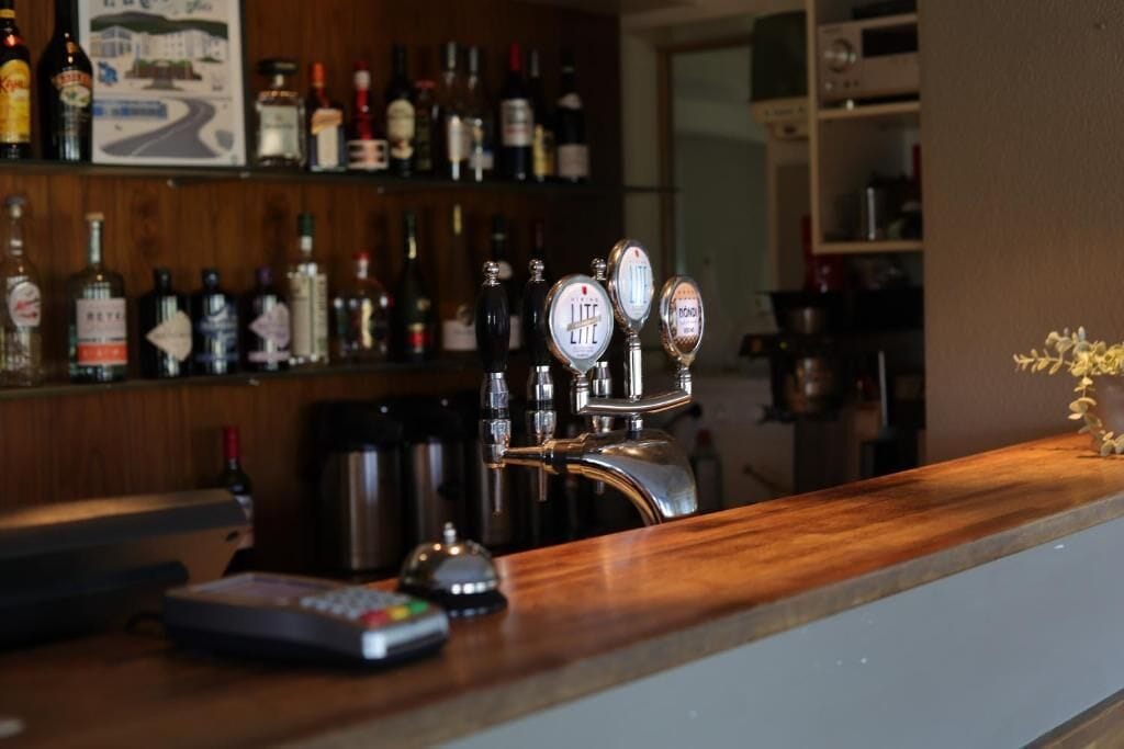 A bar area with a tap, a remote control, and a variety of bottles on shelves.