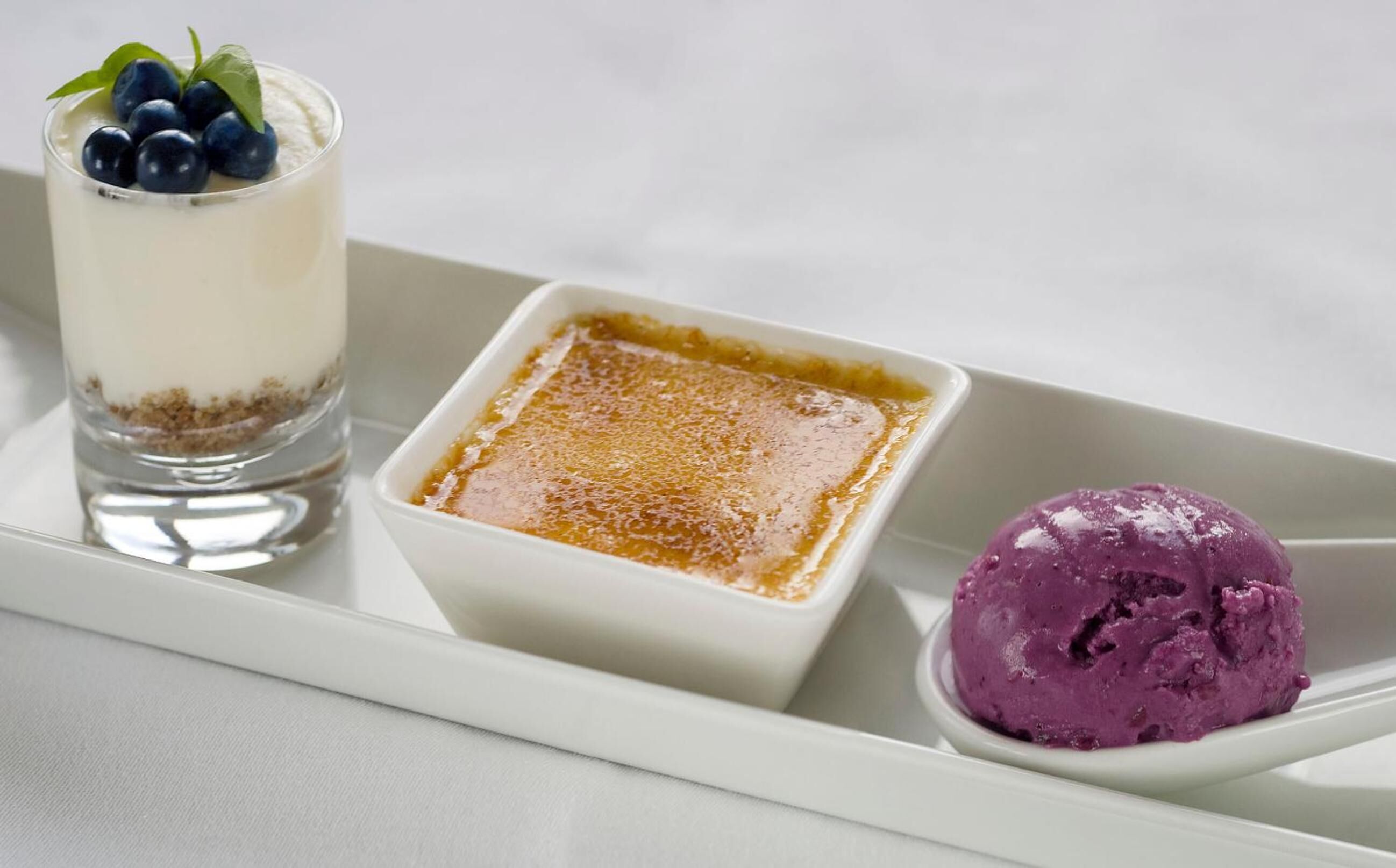 Una bandeja de postres con un parfait en capas, una tartaleta de caramelo y una porción de helado morado.