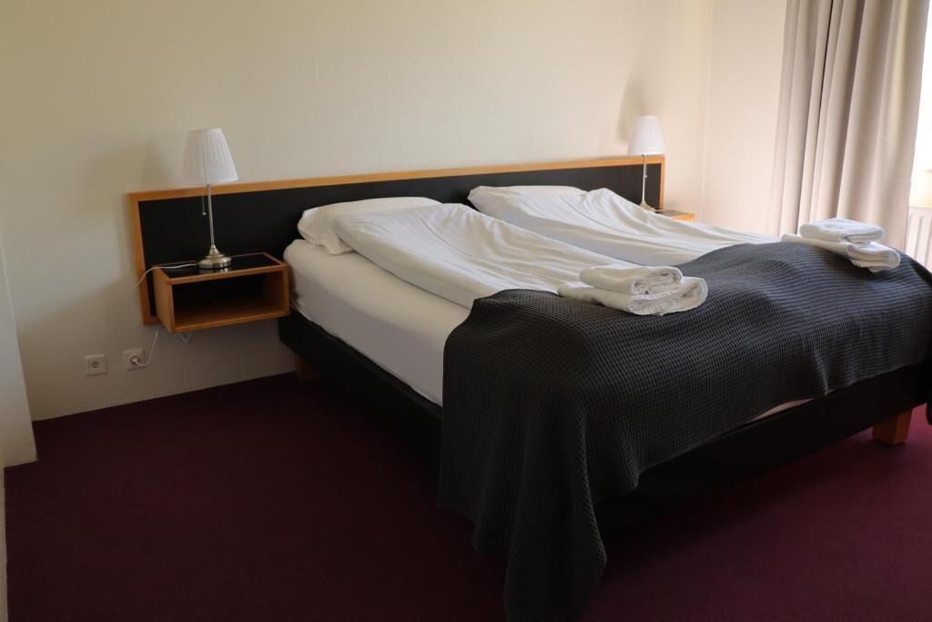 A hotel room with a bed, a nightstand, and a lamp.