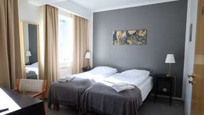 Une chambre d’hôtel avec deux lits, un bureau, une chaise, une table de chevet avec une lampe et un tableau au mur.