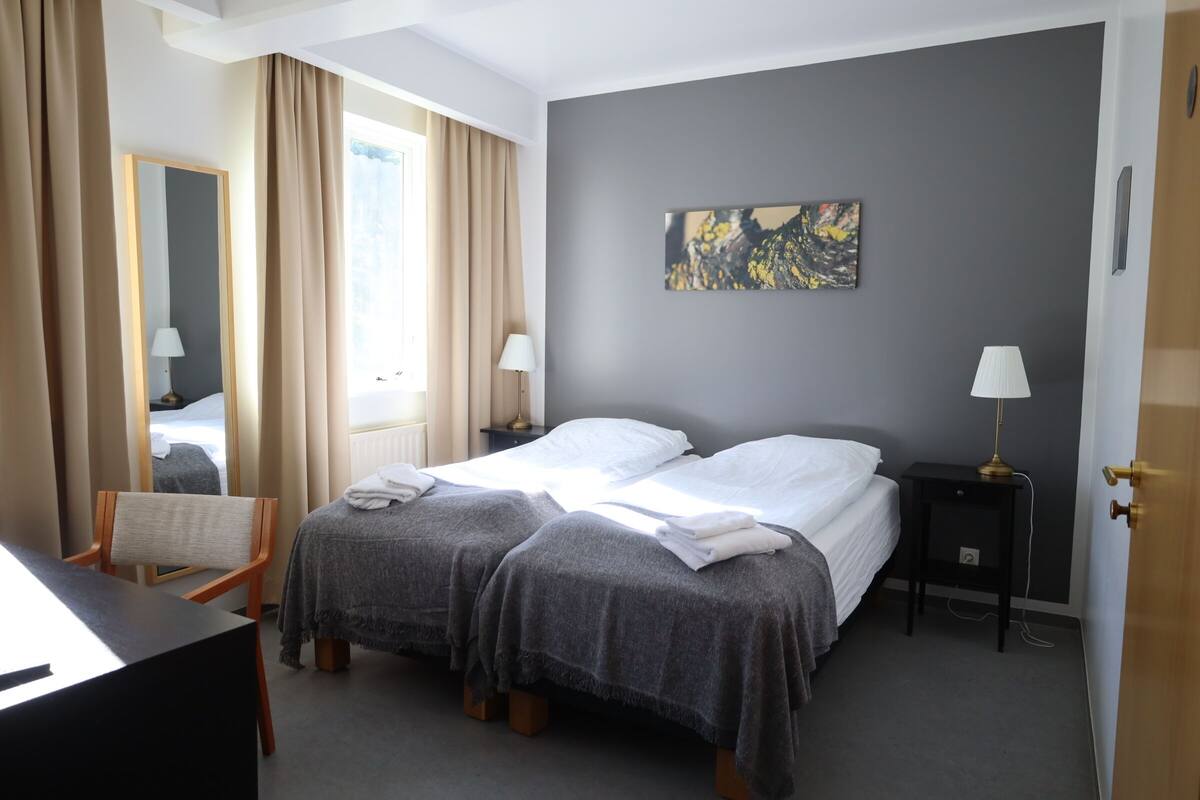 Een hotelkamer met twee bedden, een bureau, een stoel, een nachtkastje met een lamp en een schilderij aan de muur.