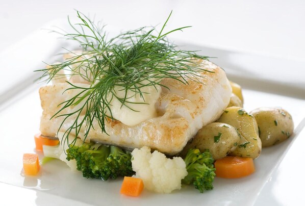 Un plato de comida con un trozo de pescado, patatas, brócoli y zanahorias.