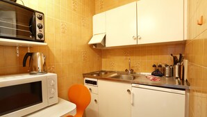 A compact kitchen with a microwave, toaster, sink, and orange chair. - Torhôtel Genève (Geneva)