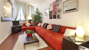 A modern living room with a red sofa, a coffee table, a TV, and a potted plant. - Torhôtel Genève (Geneva)