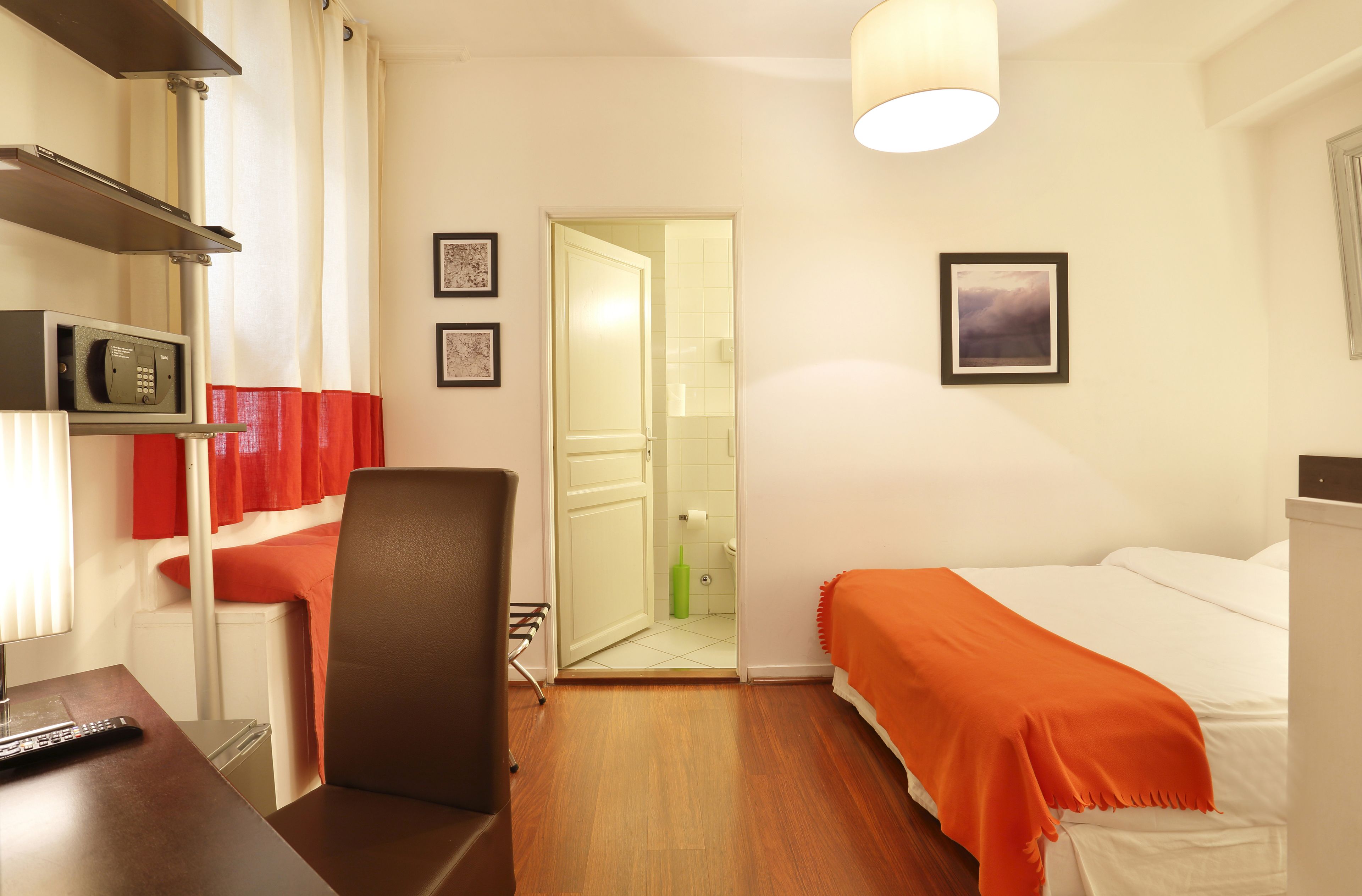 Ein Hotelzimmer mit einem Bett, einem Schreibtisch mit Fernbedienung, einem Sessel, einer Mikrowelle und einer Tür zu einem Badezimmer.