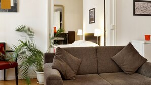 A living room with a brown sofa, a glass coffee table, a red side table, a potted plant, and a wooden floor. - Torhôtel Genève (Geneva)