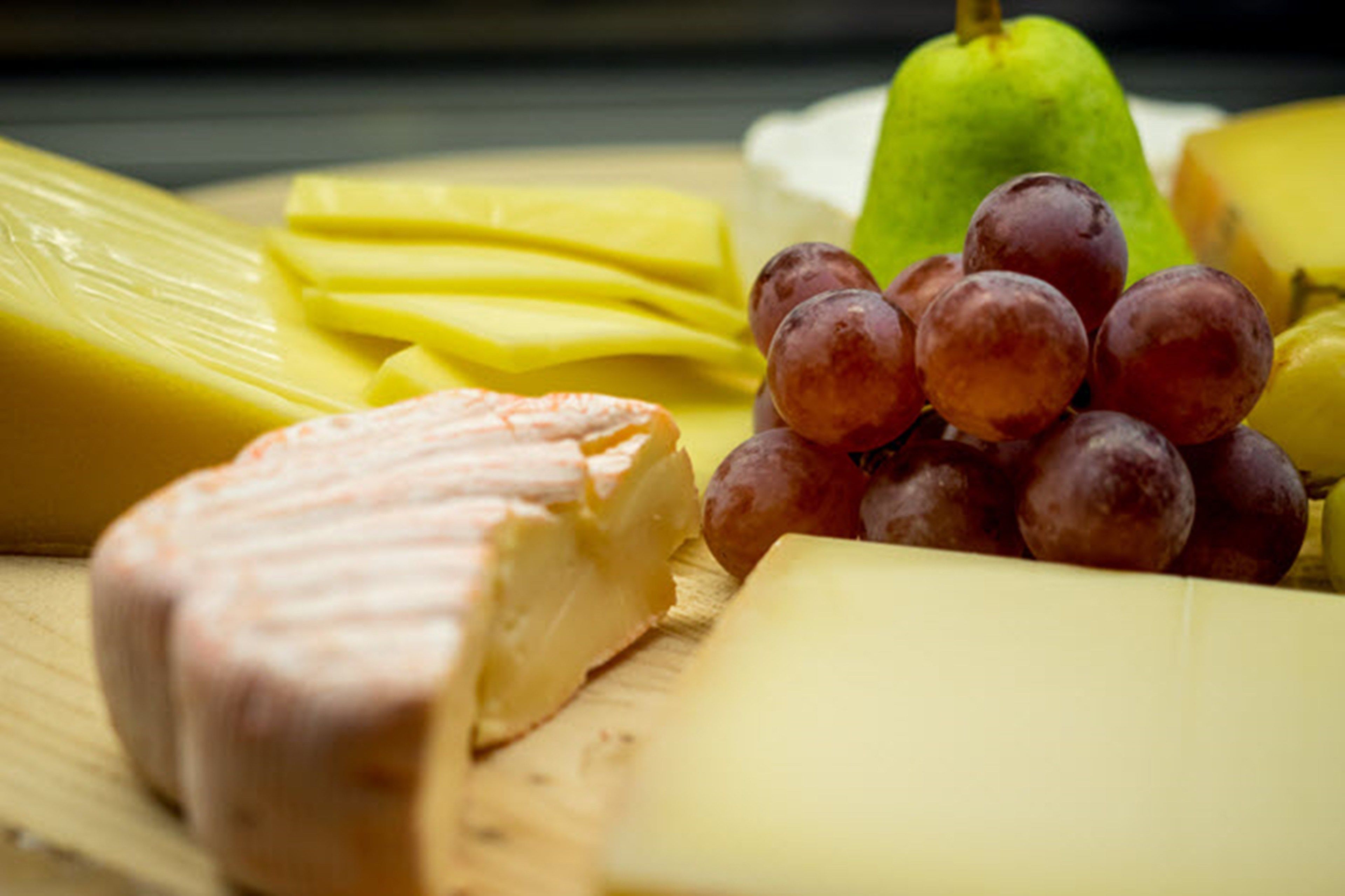 Une sélection de fromages, des raisins et une poire, présentés sur une planche en bois.